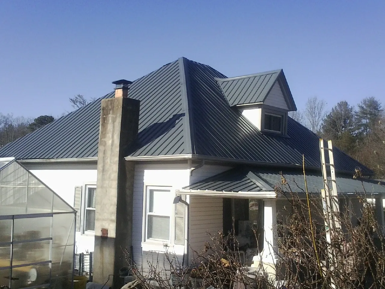 Dark blue standing seam metal roof on a white farmhouse with dormer — Slate & Tile Roof Repair by Roofing Brothers in Mebane
