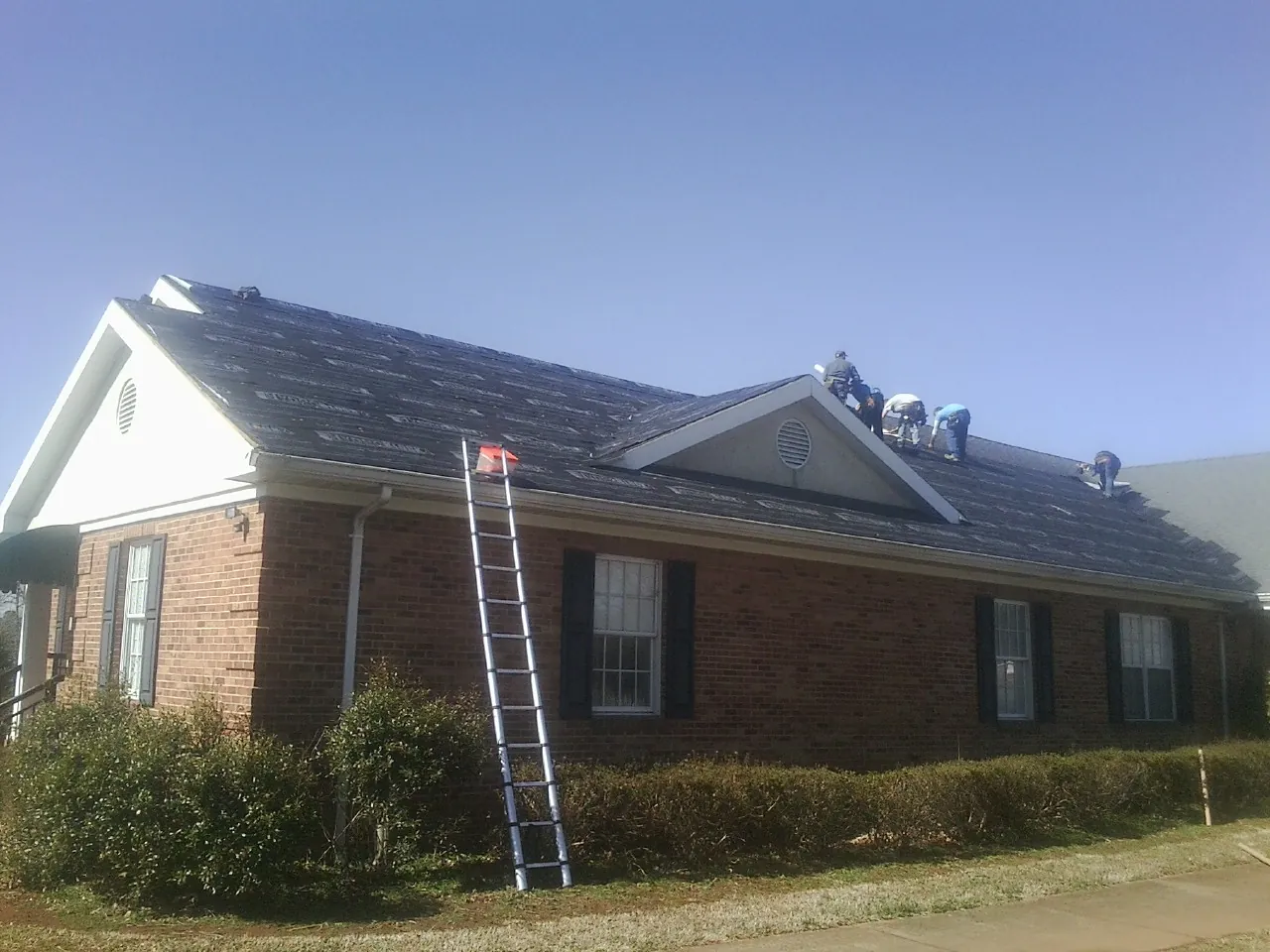 Crew tearing shingles off a brick ranch roof with a ladder set — Emergency Roof Repair work by our crew in Mebane