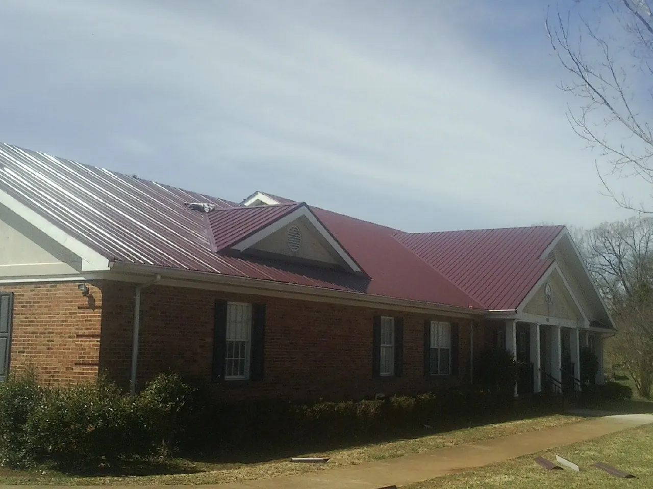 Red metal roof with gabled entries on a long brick building, from a Hail Damage Roof Repair job in Mebane