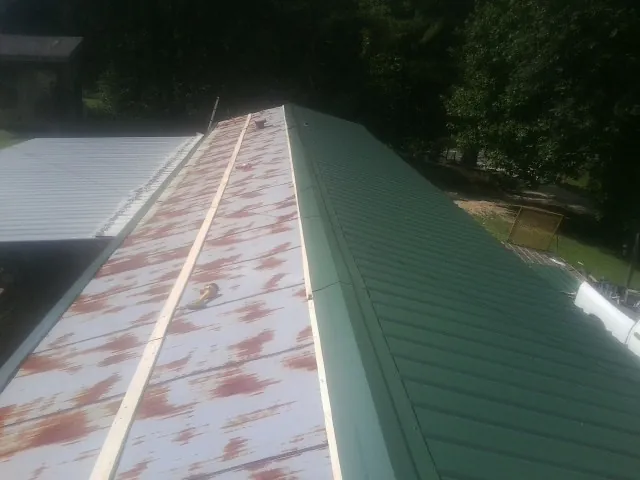 Old rusted panels beside newly installed green metal roofing — Wind Damage Roof Repair by Roofing Brothers in Mebane
