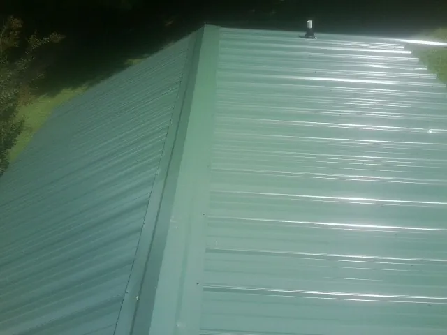 New green metal panels meeting at the ridge of a roof — Flat Roof Repair work by our crew in Mebane