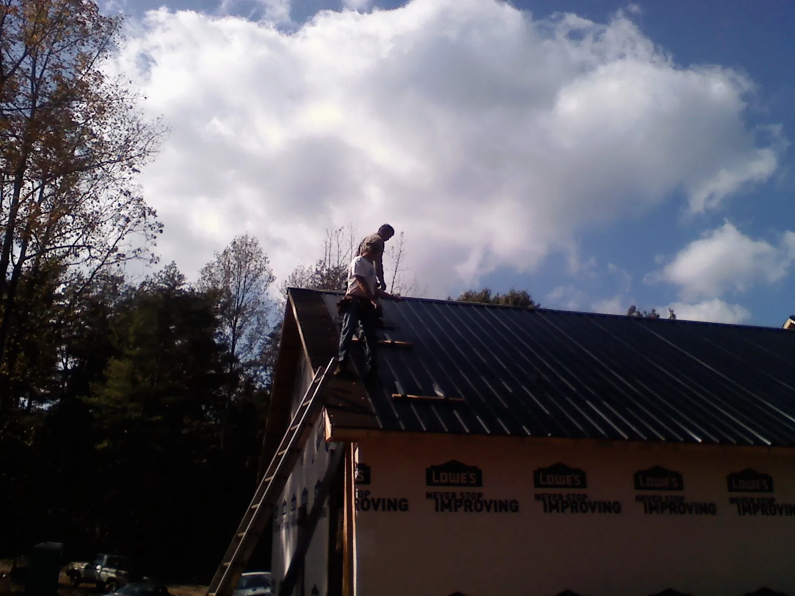 Roofer fastening dark metal panels high against a cloudy sky, from a Roof Inspection job in Mebane