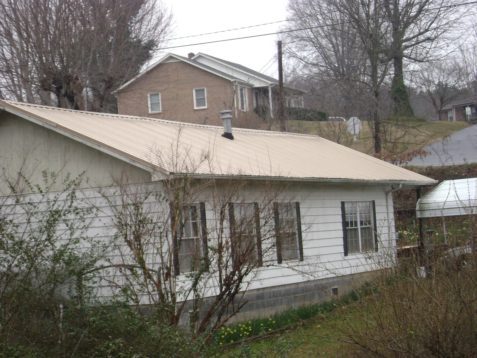 Tan metal roof on a white sided house set into a hillside — Commercial Roofing by Roofing Brothers in Mebane