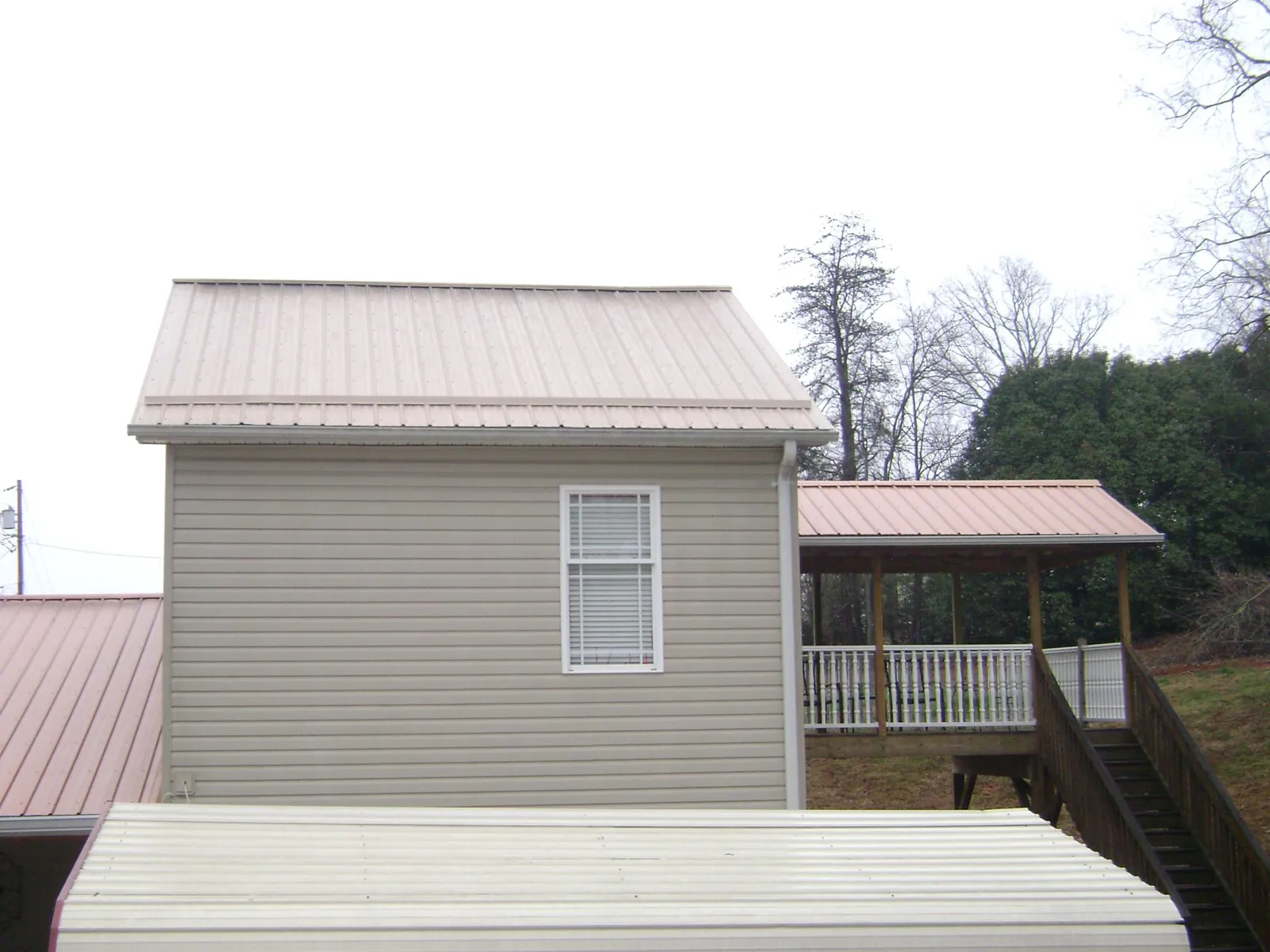 Tan metal roofs on a two story addition and attached porch, from a Roof Replacement job in Mebane